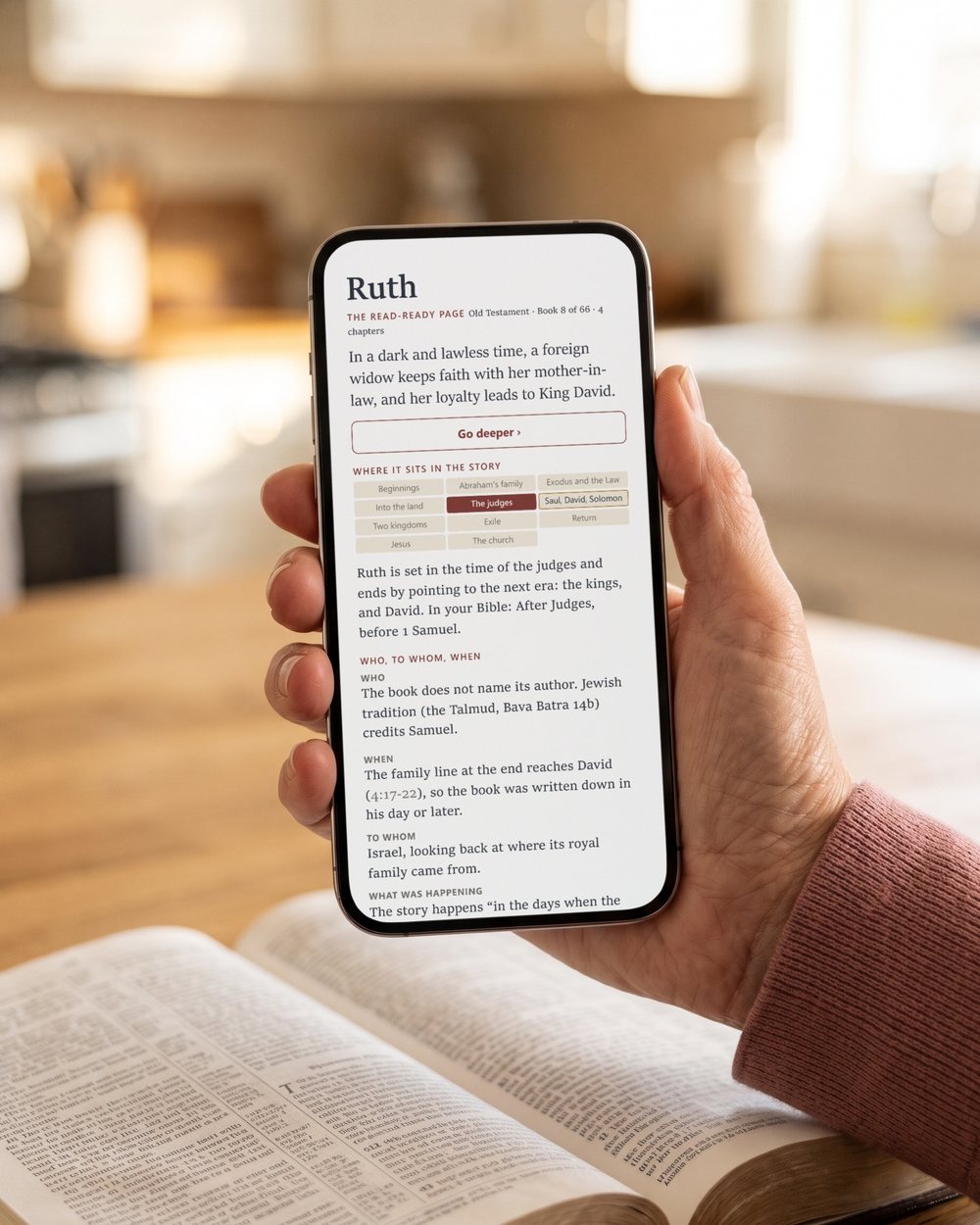A hand holding a phone with the Read-Ready page of Ruth in big print, over an open Bible